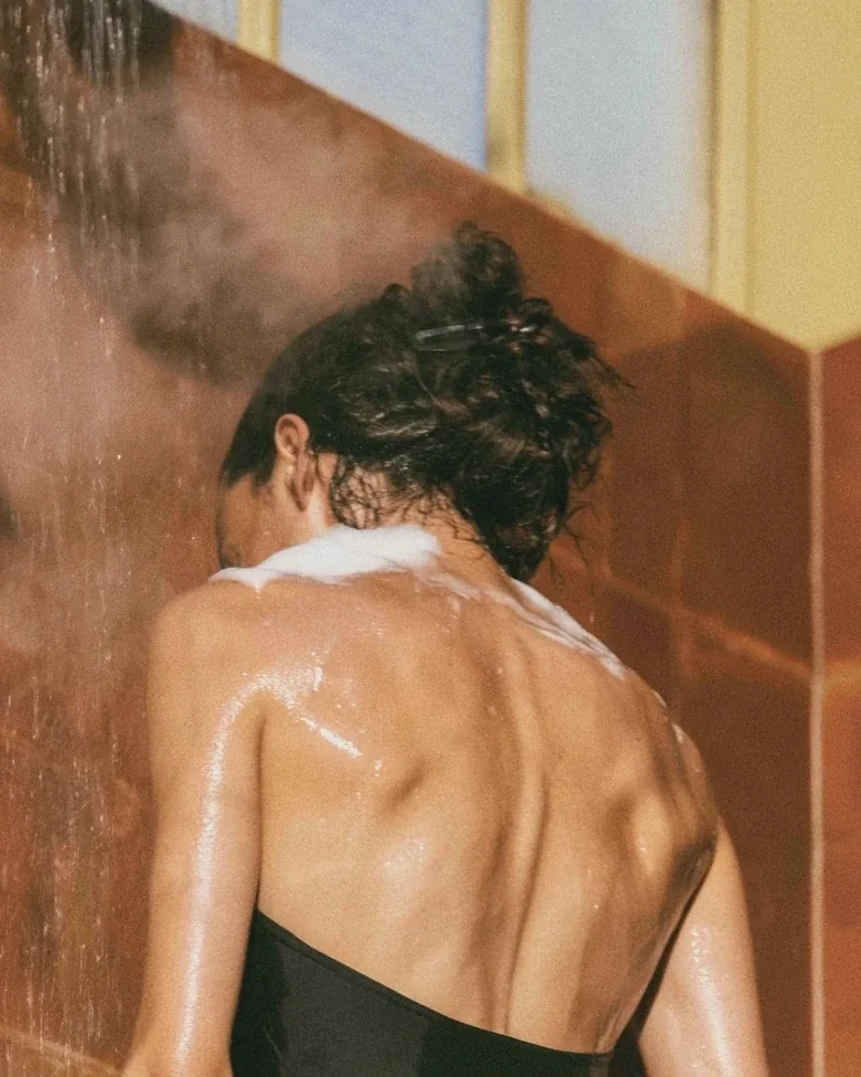 A woman’s bare back in a warm shower, sunlight on the tiles